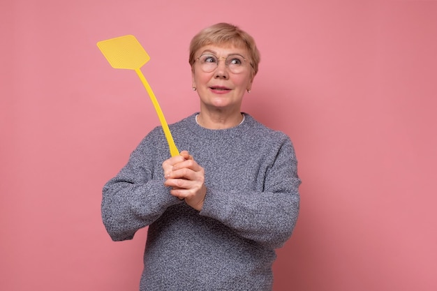 Mujer mayor caucásica con matamoscas tratando de matar a un mosquito