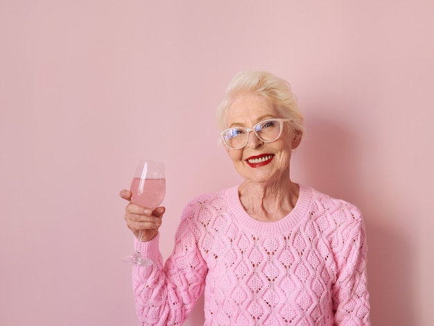 Mujer mayor caucásica en suéter rosa de cachemira bebiendo rosa sobre fondo rosa