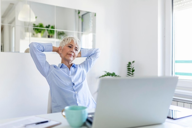 Mujer mayor centrada con el pelo blanco en casa usando la computadora portátil. Empresario senior con estilo trabajando en equipo en casa. Mujer analizando y gestionando las facturas domésticas y las finanzas del hogar.