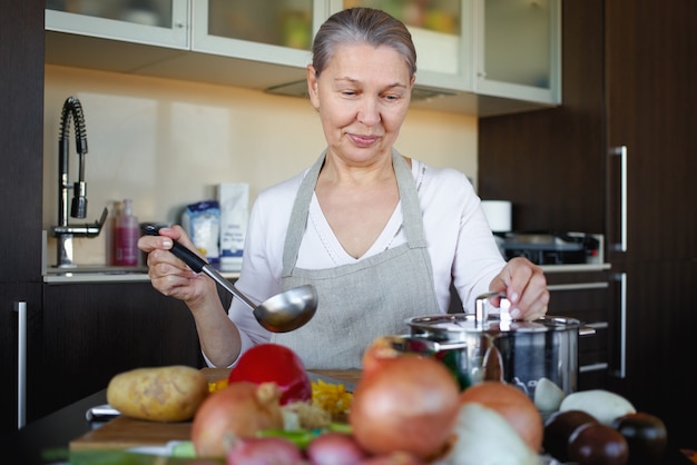 Mujer mayor en la cocina cocinando, mezclando alimentos en una olla