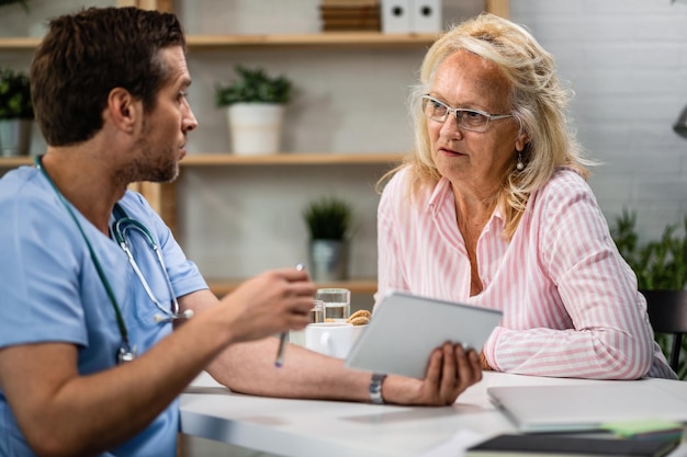 Mujer mayor comunicándose con un médico que está usando una tableta digital y explicando el resultado de su prueba médica