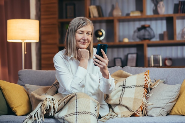 La mujer mayor descansa en las conversaciones nocturnas en videollamadas usa el teléfono y la aplicación de comunicación