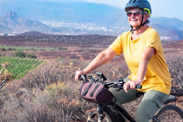 Mujer mayor despreocupada en excursión al aire libre en su bicicleta eléctrica Viñedo verde y montaña en segundo plano.