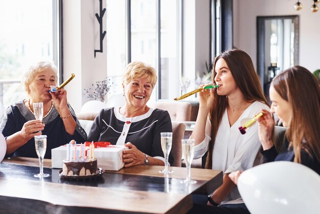 Mujer mayor con familiares y amigos celebrando un cumpleaños en el interior.