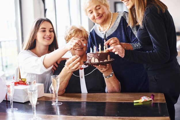 Mujer mayor con familiares y amigos celebrando un cumpleaños en el interior.