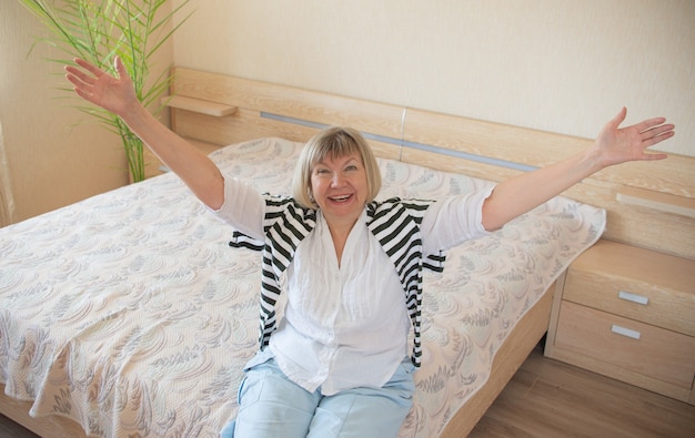 Foto mujer mayor feliz con cabello gris relajante sonriendo está mirando a la cámara en su casa en el dormitorio.