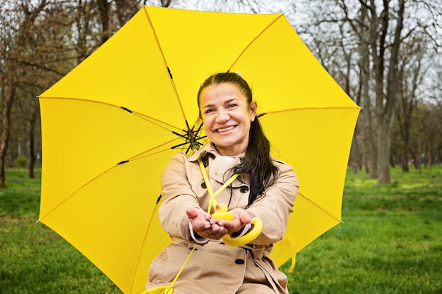 Mujer mayor feliz en capa de lluvia amarilla con paraguas amarillo caminando en el parque ancianos maduros alegres