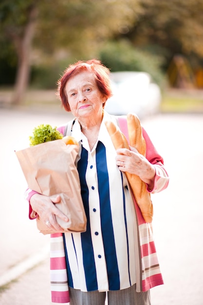 Mujer mayor feliz con pan fresco y comida en una bolsa de papel