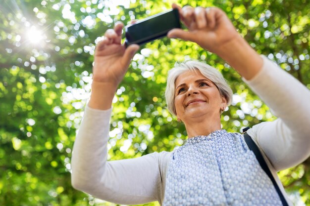 Foto mujer mayor fotografiando por celda en el parque de verano