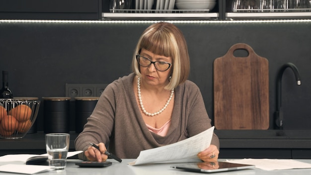 Mujer mayor con gafas considera gastos en calculadora