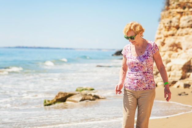 Mujer mayor con gafas de sol se para en la playa y mira al mar