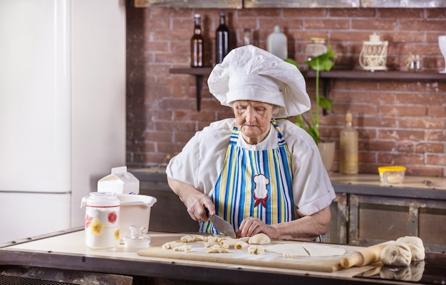 Mujer mayor en gorro de cocinero preparando pasteles en la cocina de casa