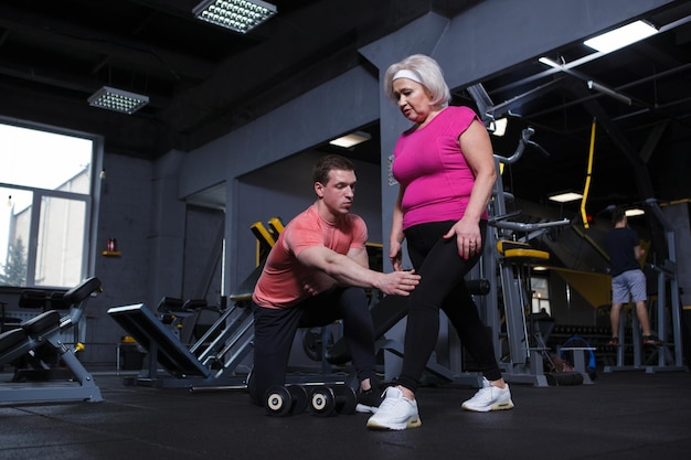 Mujer mayor haciendo estocadas bajo la supervisión de un entrenador personal en el gimnasio