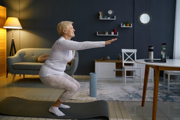 Mujer mayor haciendo sentadillas haciendo ejercicio en casa