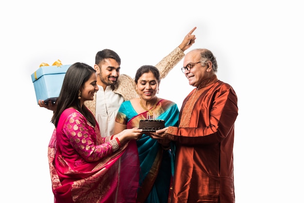 Mujer mayor india con la familia celebrando un cumpleaños soplando velas en la torta mientras usa ropa étnica