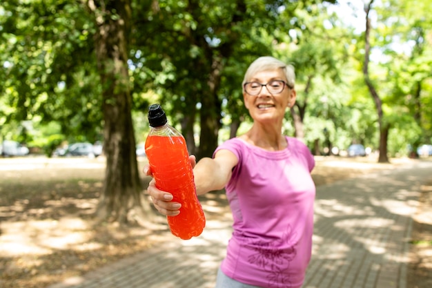 Mujer mayor lista para entrenar con bebida energética en el parque.