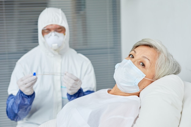 Foto mujer mayor, llevando, máscara, acostado, cama, en, hospital, con, doctor, en, protector, uniforme, sentado, atrás