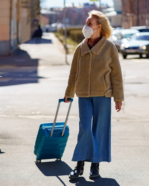 Mujer mayor con maleta azul viajando sola durante la epidemia de coronavirus