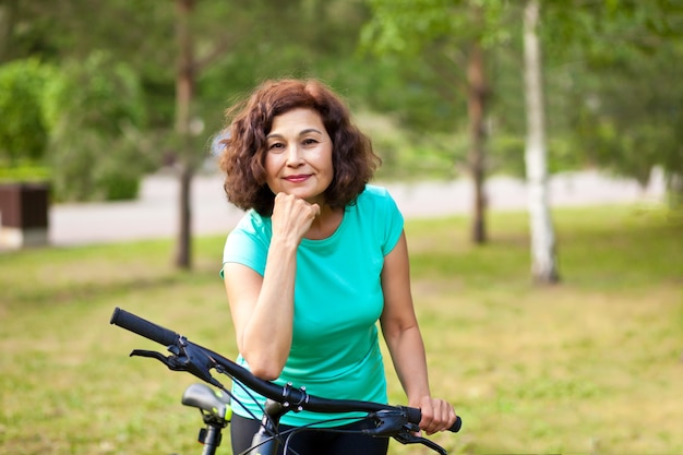 Mujer mayor de mediana edad en bicicleta en el parque de campo al aire libre.