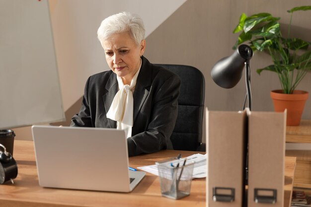 Mujer mayor de mediana edad europea con estilo segura que usa una computadora portátil en el lugar de trabajo Mujer de negocios de cabello gris de los años 60 madura y elegante sentada en la mesa de la oficina Trabajadora profesional de maestro líder jefe