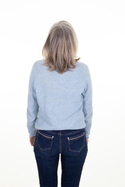 Mujer mayor de mediana edad con suéter azul y pantalones de mezclilla sobre un fondo blanco Vista posterior de la dama de pelo gris trasero