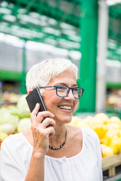 Mujer mayor en mercado usando el teléfono móvil