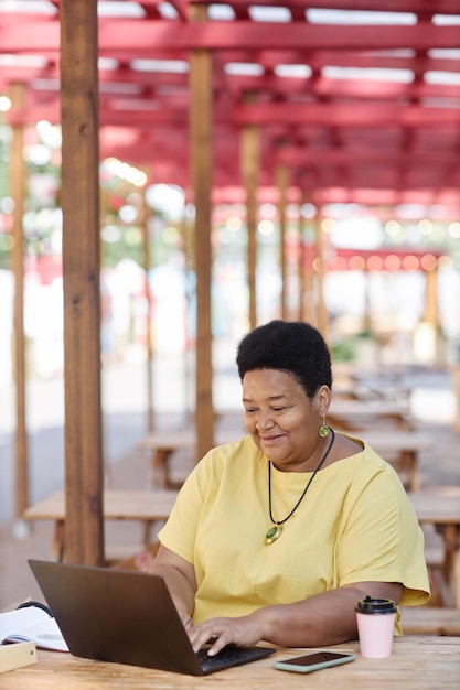 Mujer mayor negra usando una computadora portátil en un café al aire libre y sonriendo