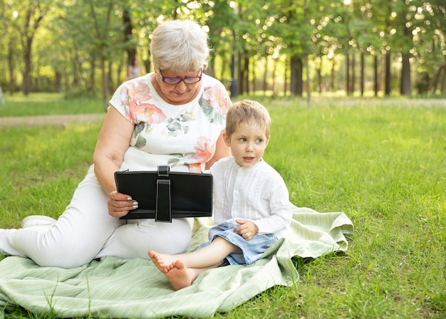 Mujer mayor y nieto con dispositivo inteligente para comprar en línea en el parque