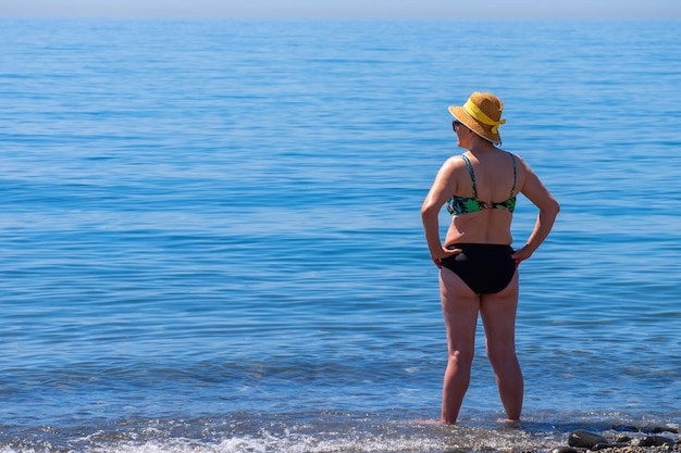 Mujer mayor parada sola frente al mar mediterráneo en una playa en un día soleado de verano