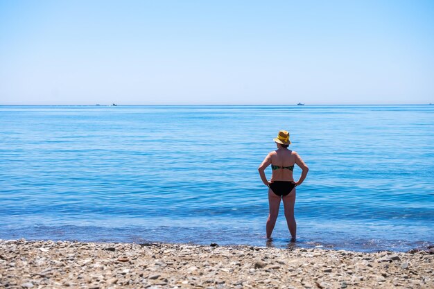 Mujer mayor parada sola frente al mar mediterráneo en una playa en un día soleado de verano