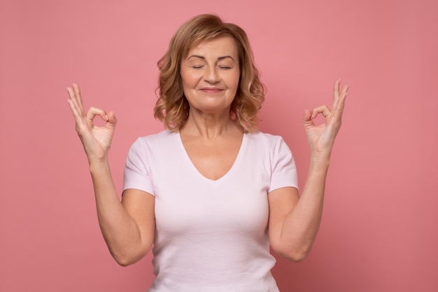 Mujer mayor que mantiene los ojos cerrados mientras medita estar tranquila y pacífica tomándose de la mano en mudra