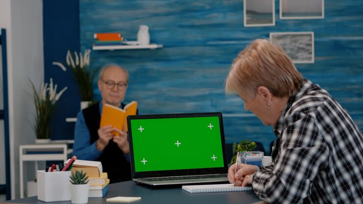 Foto mujer mayor que mira el monitor de pantalla verde que trabaja desde casa tomando notas en el cuaderno ...
