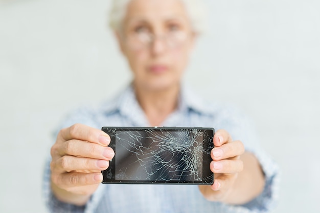 Foto mujer mayor que muestra smartphone con la pantalla agrietada