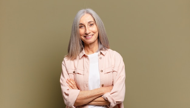 Mujer mayor que parece un cumplidor feliz, orgulloso y satisfecho sonriendo con los brazos cruzados