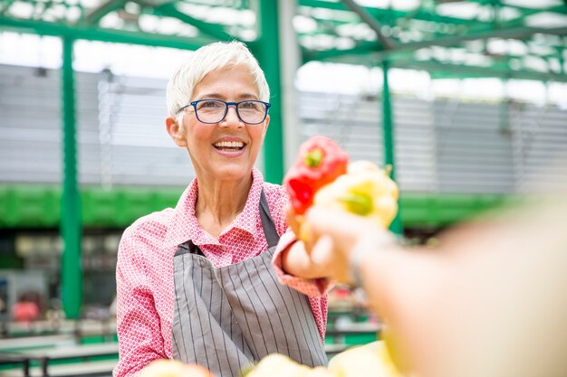 La mujer mayor que parece que lleva los vidrios vende la pimienta en mercado