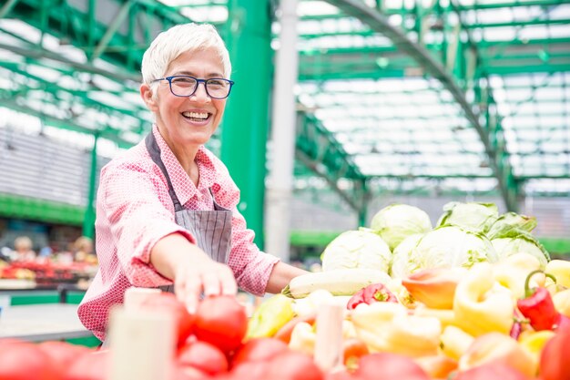 La mujer mayor que parece que lleva los vidrios vende la pimienta en mercado