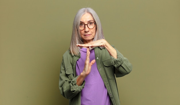 Mujer mayor que parece seria, severa, enojada y disgustada, haciendo el signo de tiempo de espera