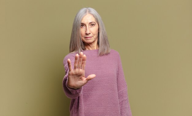 Mujer mayor que parece serio, severo, disgustado y enojado mostrando la palma abierta haciendo gesto de parada