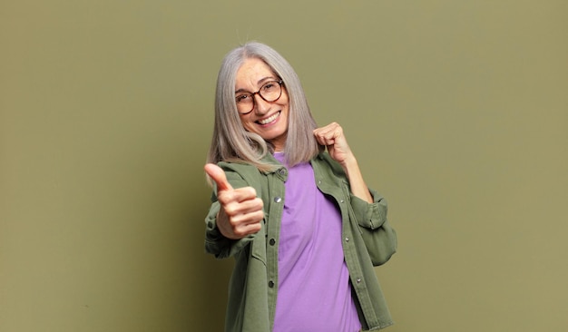 Mujer mayor que se siente orgullosa, despreocupada, segura y feliz, sonriendo positivamente con los pulgares hacia arriba