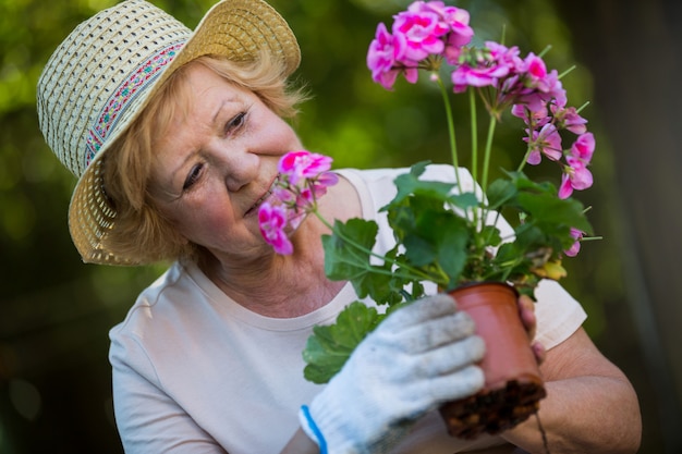Mujer mayor que sostiene la planta de tiesto en jardín