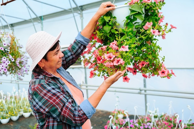 Foto una mujer mayor que trabaja en un invernadero examina cuidadosamente las ollas de flores en la vista lateral del