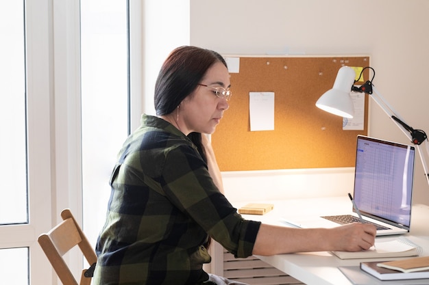 Mujer mayor que usa la computadora portátil en la oficina en casa.