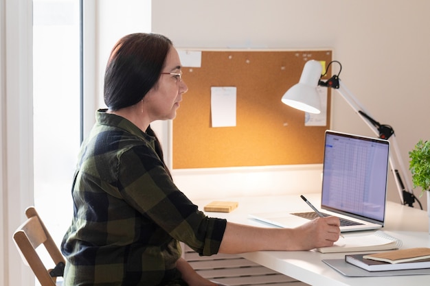 Mujer mayor que usa la computadora portátil en la oficina en casa.