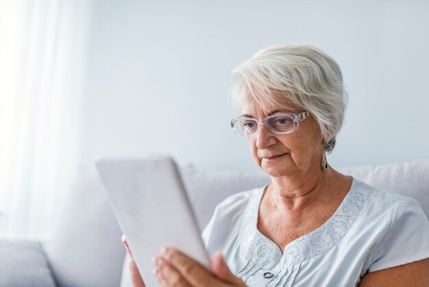 Mujer mayor que usa la tableta digital en casa
