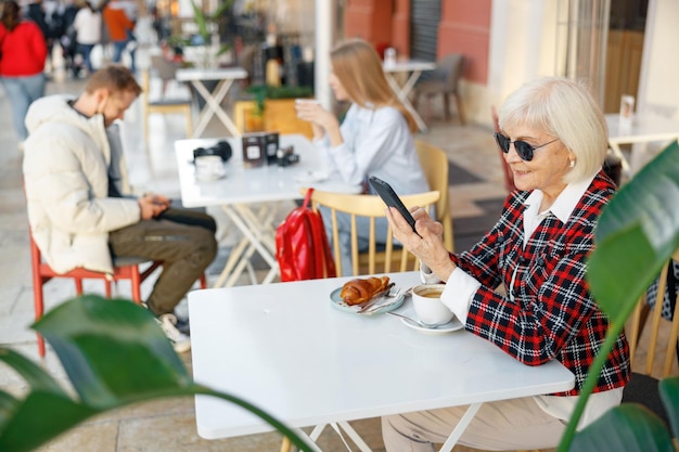 Mujer mayor que usa el teléfono celular mientras almuerza en la cafetería