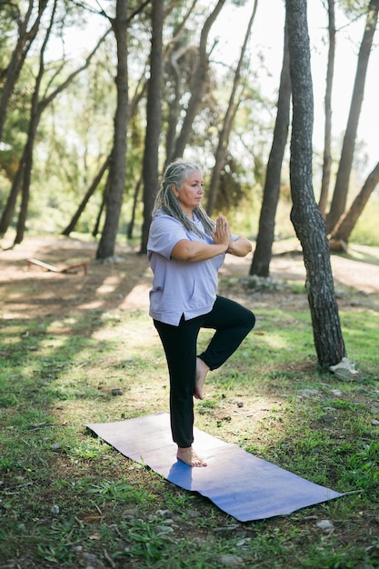 Mujer mayor con rastas en posición de estiramiento en la naturaleza por la mañana Mujer mayor haciendo yoga en el parque bienestar y bienestar tai chi