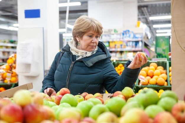 Mujer mayor recogiendo manzana en la tienda de comestiblesxDxAxDxA