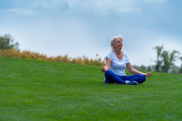 Mujer mayor relajándose sobre la hierba verde durante la meditación