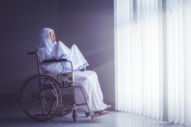Mujer mayor rezando a Alá en silla de ruedas