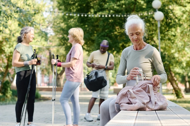 Foto mujer mayor sentada en un banco y empacando cosas en una bolsa después del entrenamiento deportivo al aire libre